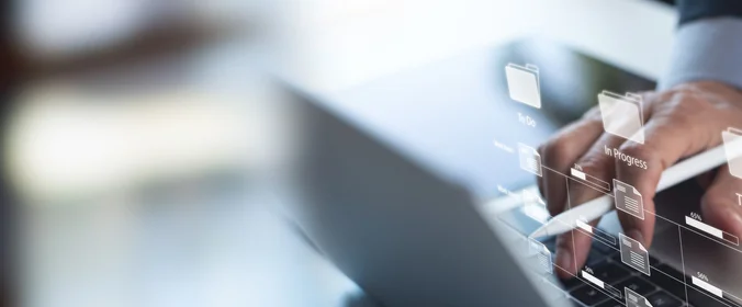 foto de uma mão mexendo em um notebook com alguns hologramas de pastas em cima